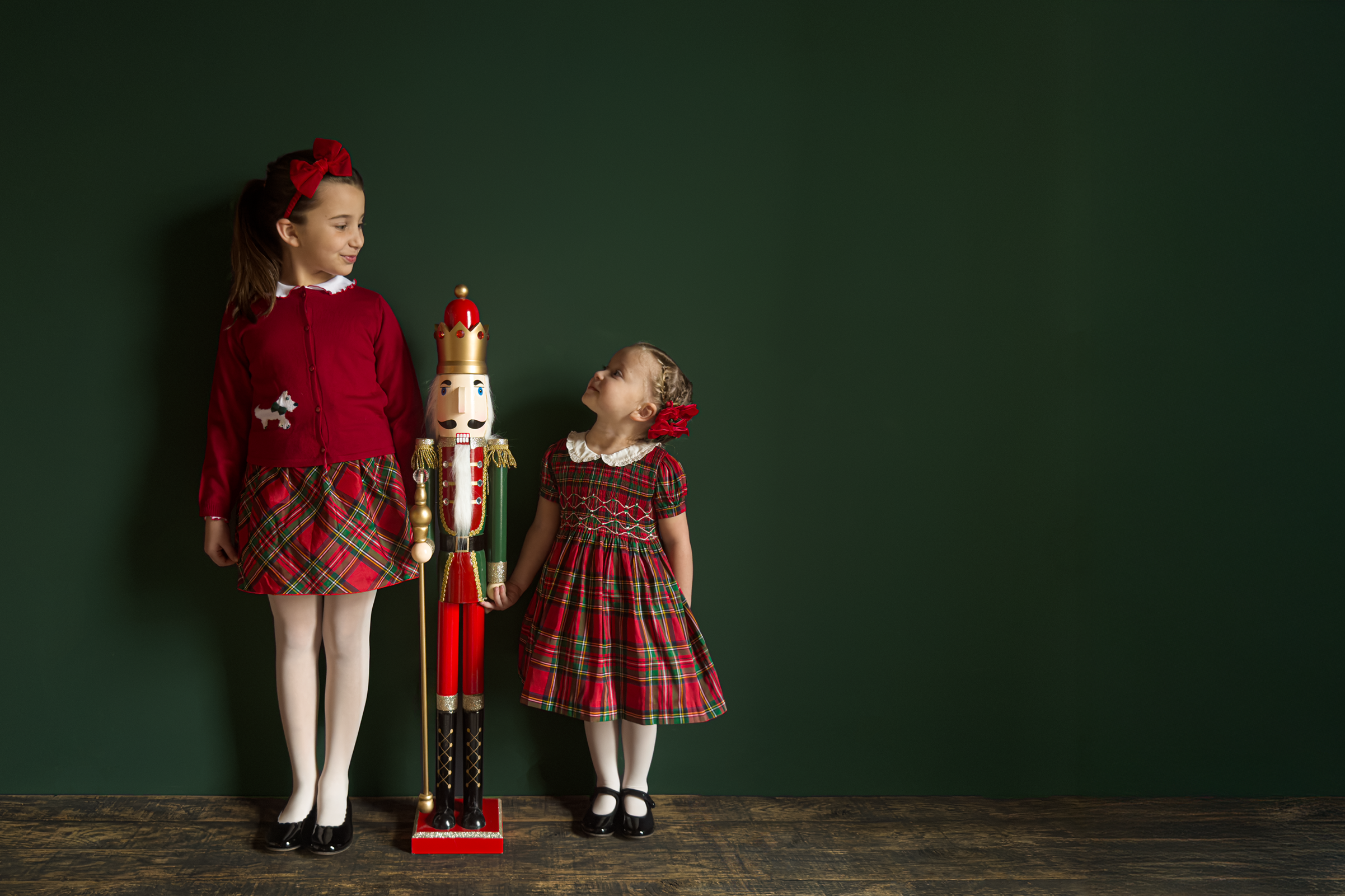 Two children in matching outfits standing next to a large nutcracker against a dark green background