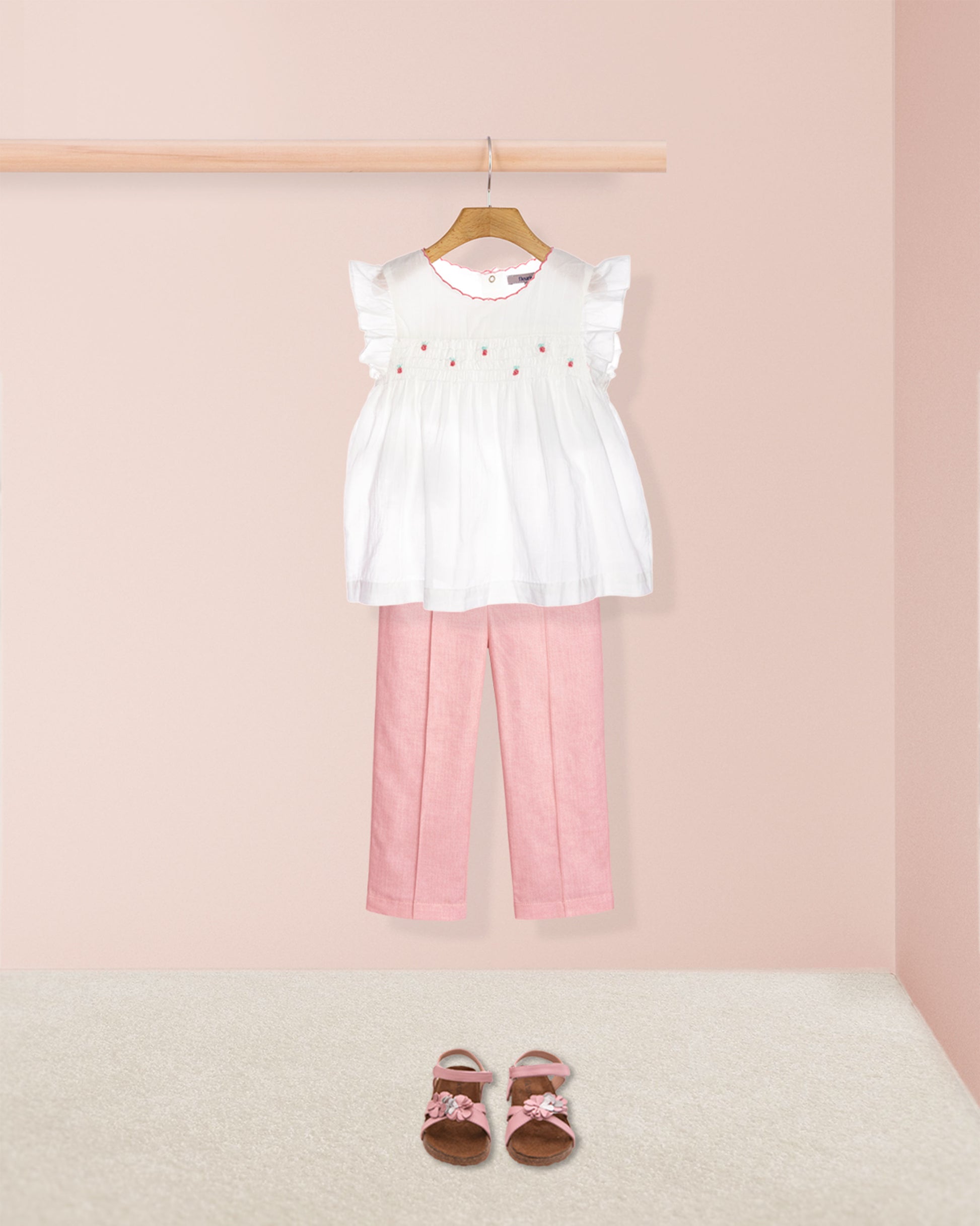 White top with ruffled sleeves and pink pants on a hanger against a pink background.