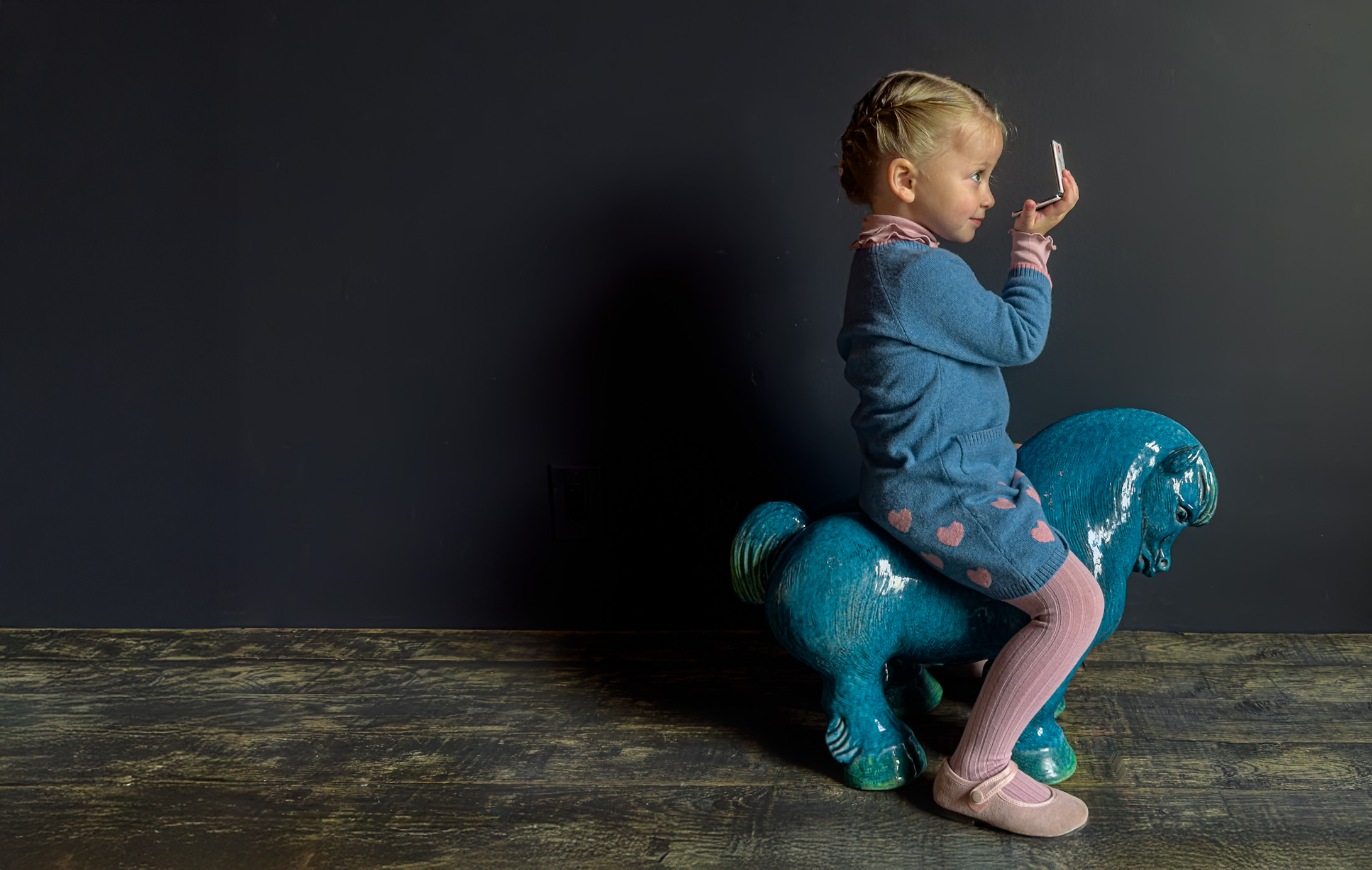 Child sitting on a blue toy horse against a dark background