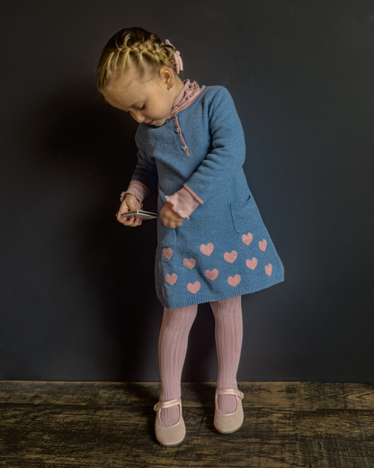 Young girl in a blue dress with pink hearts standing against a dark background