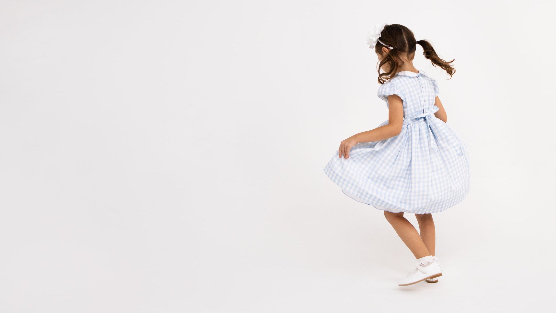 girl turned around dancing, wearing a light blue and white checkered dress, white shoes and pig tails