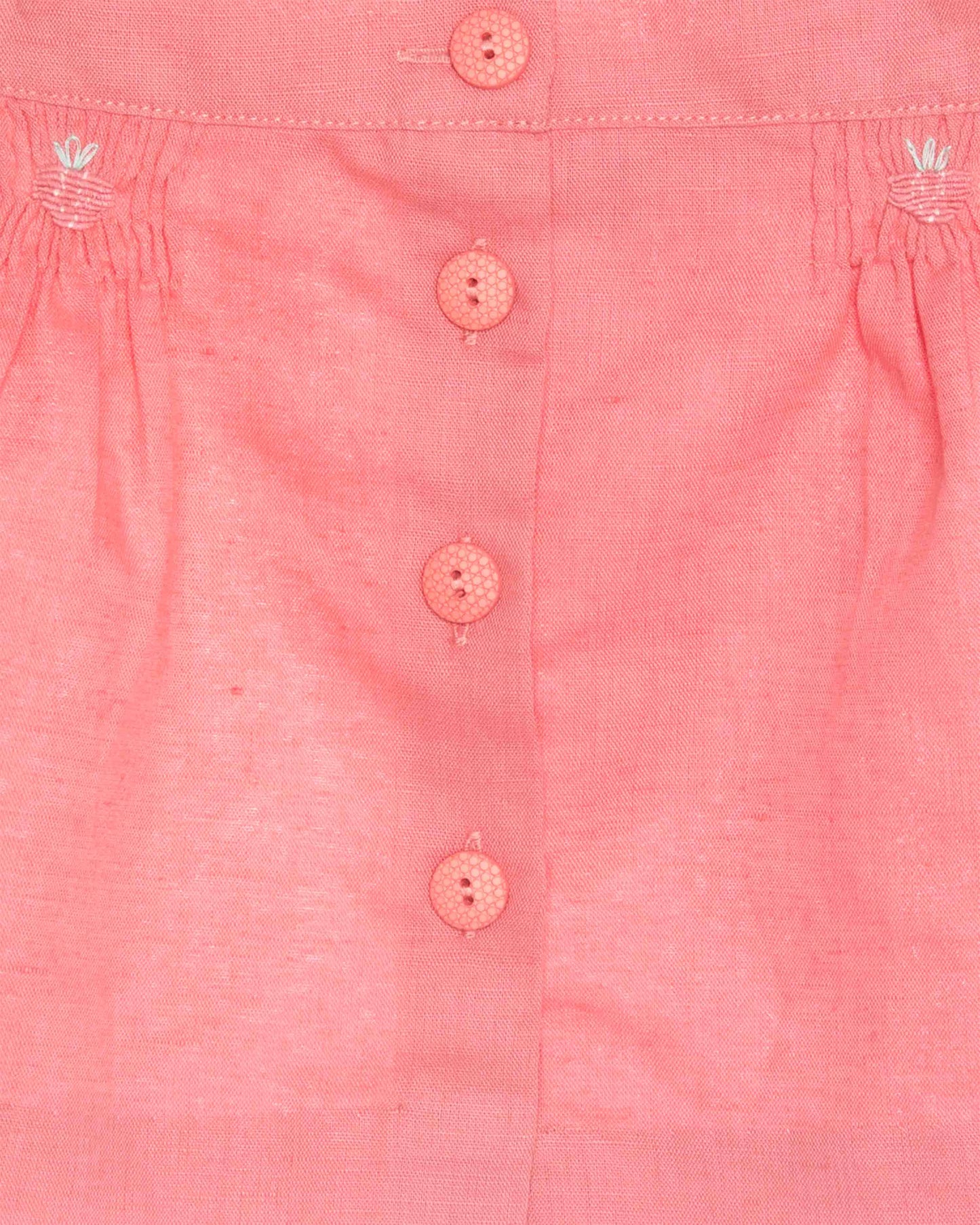 Close-up of a pink shirt with buttons and floral patterns on a light background