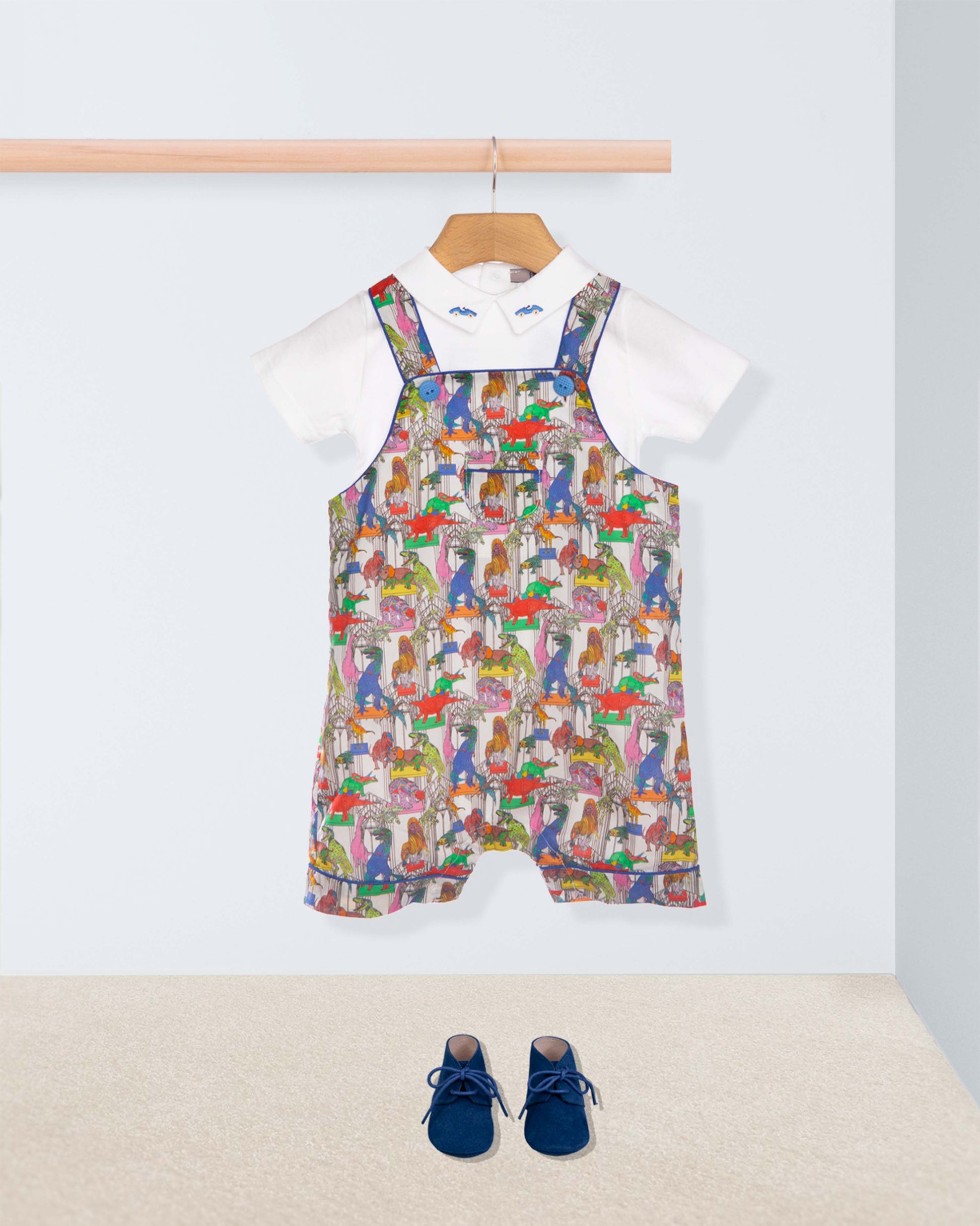 Colorful patterned overalls on a hanger with a white shirt underneath, on a light gray background.