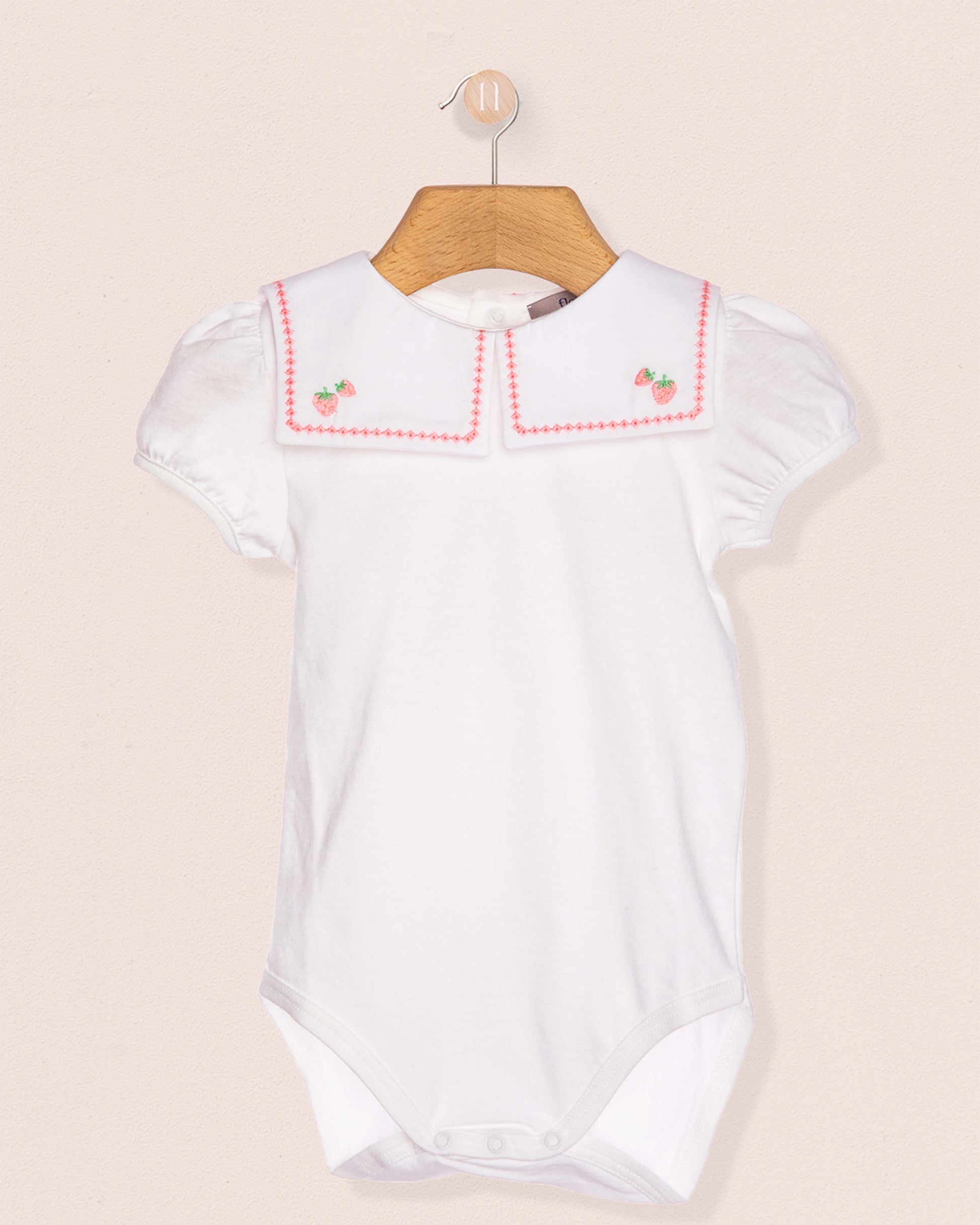 White baby romper with red trim on a beige background
