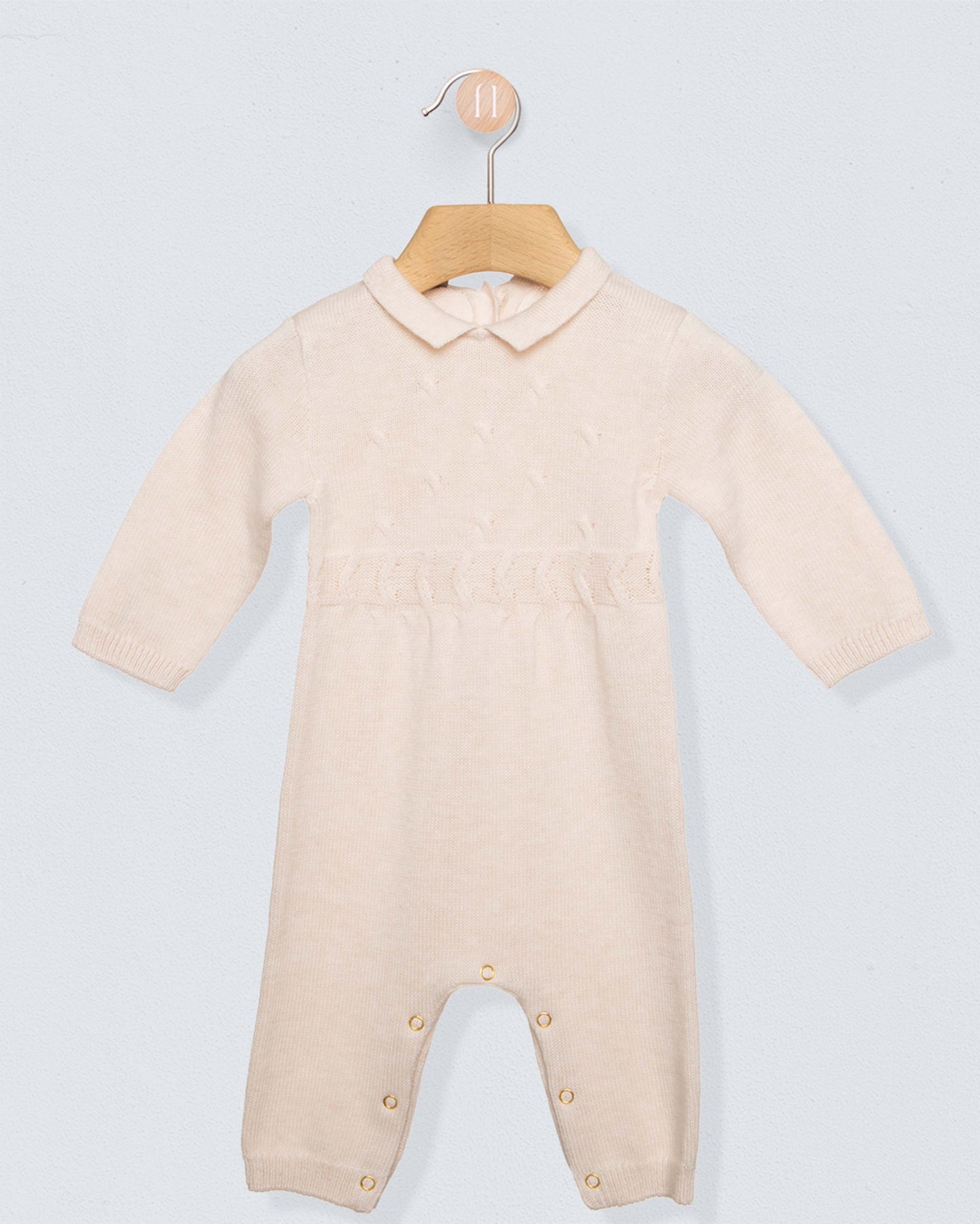 Oatmeal beige colored onesie romper with buttons on leg seams and a collar, on a hanger against a grey background