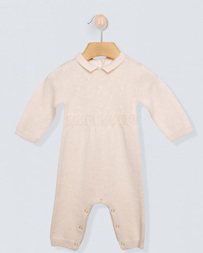 Oatmeal beige colored onesie romper with buttons on leg seams and a collar, on a hanger against a grey background