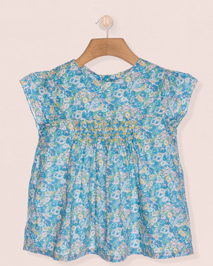 Floral-patterned blue top on a hanger against a beige background