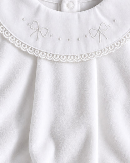 Close-up of a white baby garment featuring a decorative lace collar with embroidered bow details and a snap button at the neckline.