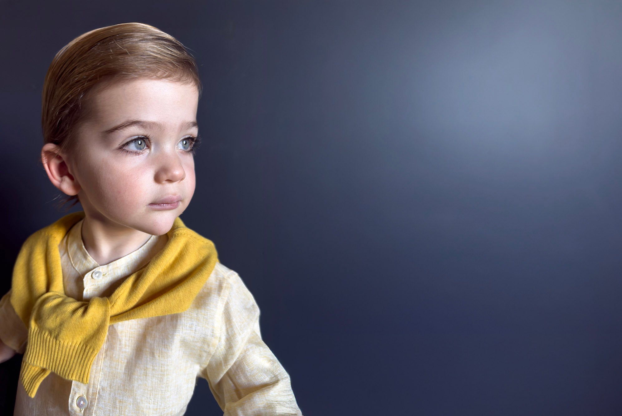 Child wearing a yellow sweater draped around shoulders and yellow shirt, against a dark background