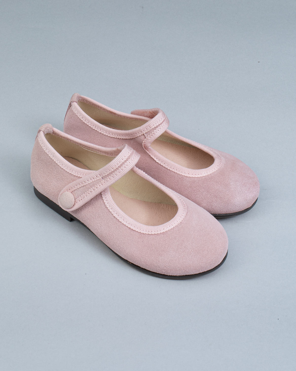 Pair of Elizabeth Pink Suede Mary-Jane shoes with velcro straps and tonal trim, placed side by side on a gray backdrop.