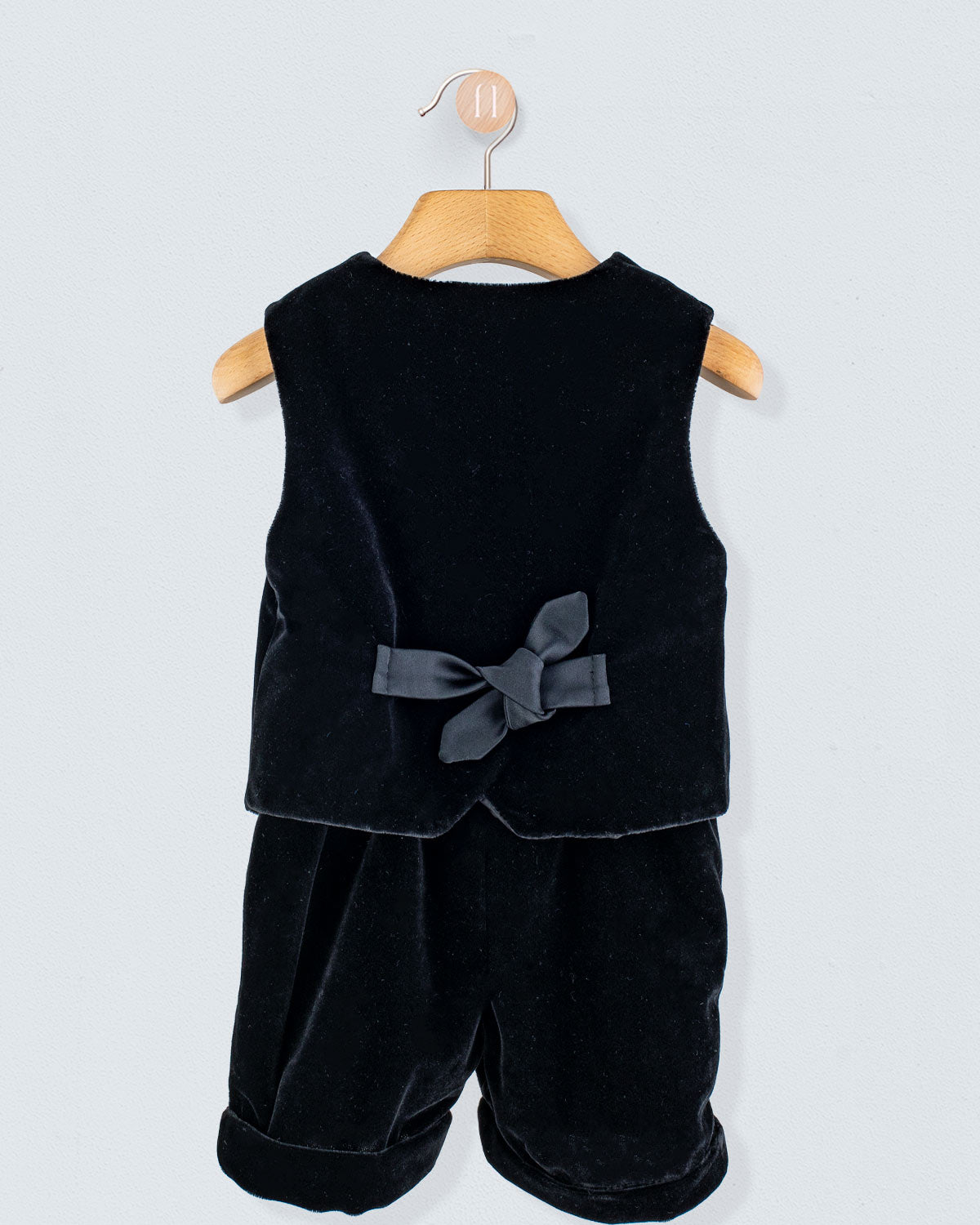Adam 2-Piece Black Velvet Vest and Suspender Shorts on a hanger, showcasing the sleeveless vest with a back bow and matching shorts with cross-back suspenders.