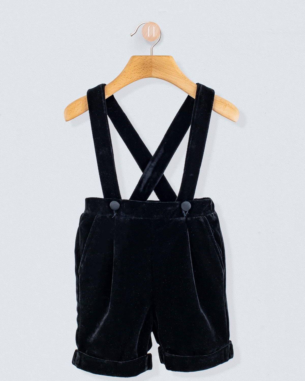 Adam 2-Piece Black Velvet Vest and Suspender Shorts, featuring cross-back suspenders, rolled cuffs, and satin buttons, hanging on a wooden hanger.