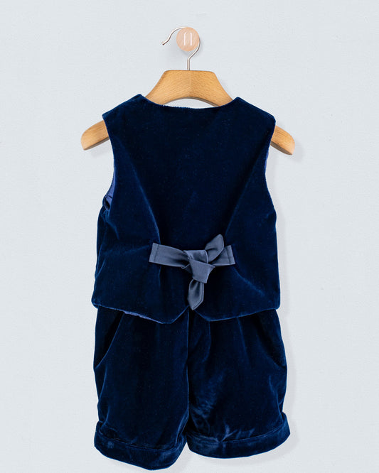 Adam 2-Piece Navy Velvet Vest and Suspender Shorts on wooden hanger, showcasing a sleeveless vest with a fabric bow and matching shorts with cross-back suspenders.