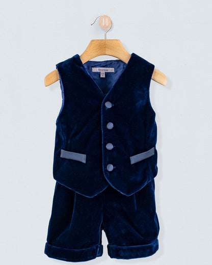 Adam 2-Piece Navy Velvet Vest and Suspender Shorts on a wooden hanger, featuring a button-front vest with faux pockets and matching cuffed shorts with suspenders.