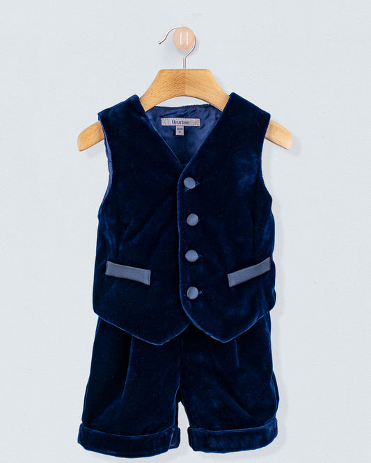 Adam 2-Piece Navy Velvet Vest and Suspender Shorts on a wooden hanger, featuring a button-front vest with faux pockets and matching cuffed shorts with suspenders.