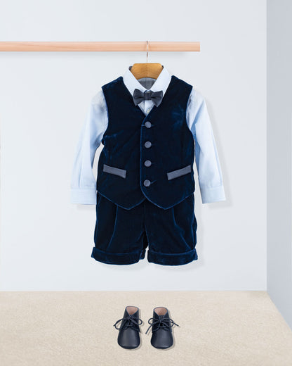 Adam 2-Piece Navy Velvet Vest and Suspender Shorts displayed with a light-blue shirt, bow tie, and toddler shoes, showcasing elegant, Italian-crafted formalwear.