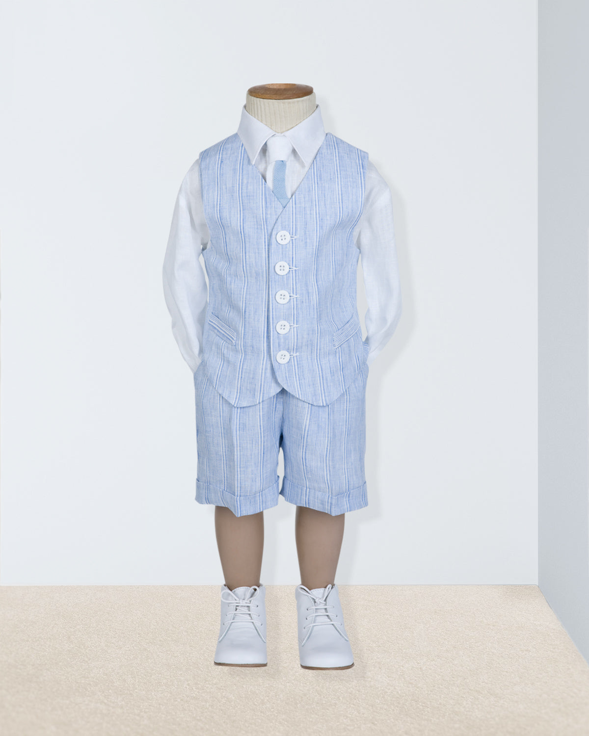 Front view of blue striped linen vest and suspender shorts set styled over a white button-down shirt on a child-sized mannequin