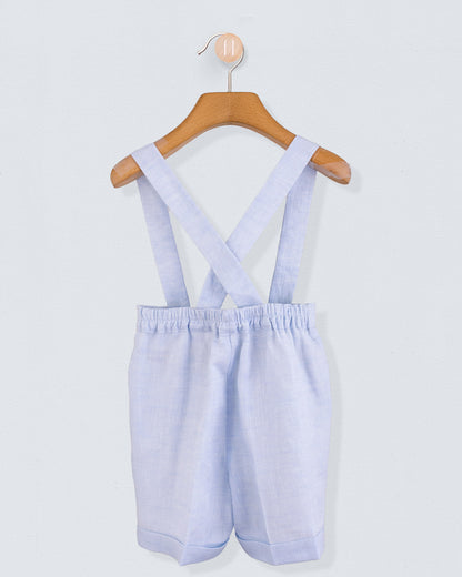 Back view of light blue linen suspender shorts with crossed straps and elastic waistband, hanging on a wooden hanger