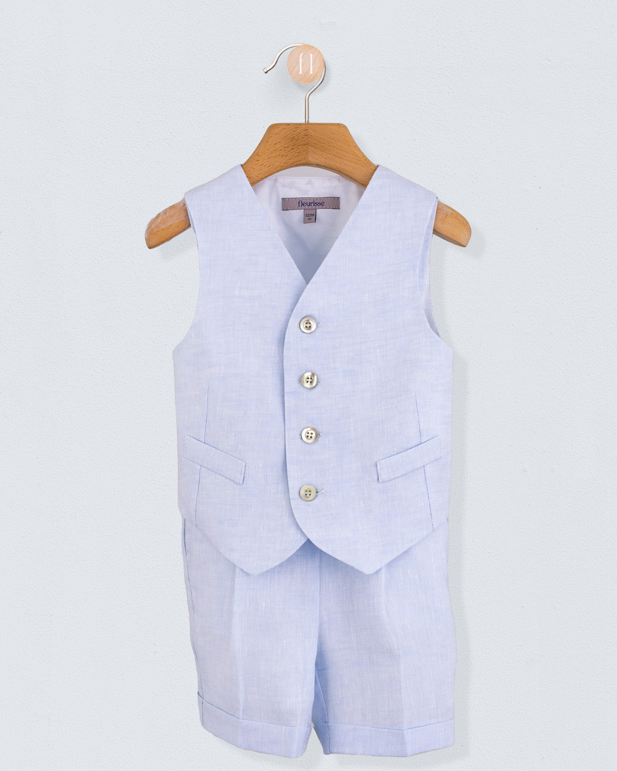 Front view of light blue linen vest and matching suspender shorts set, displayed on a wooden hanger.