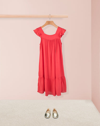 Coral ruffle dress styled with metallic toddler shoes hanging on a wooden hanger. 