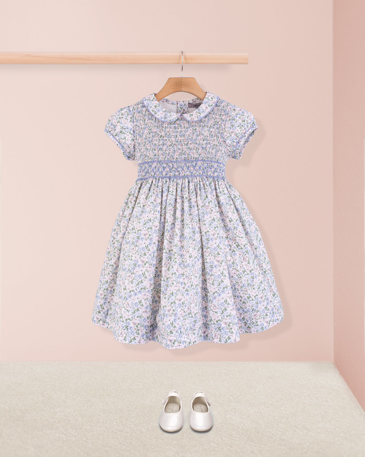 Amanda Lauren Blue Floral Smocked Dress styled with white shoes hanging on a hanger