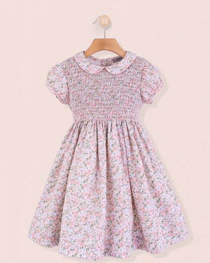 Pink floral smocked dress hanging on wooden hanger