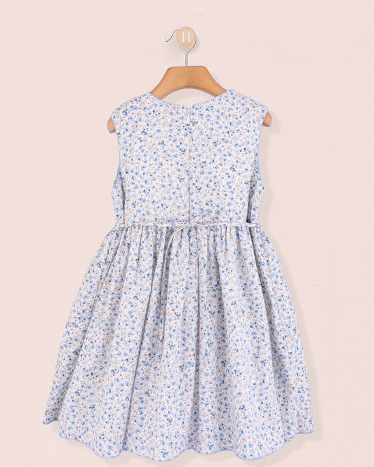 Back view of the Amandine Florencia Blue Floral Dress showing a zipper closure and fully gathered skirt in light blue floral fabric, displayed on a wooden hanger.