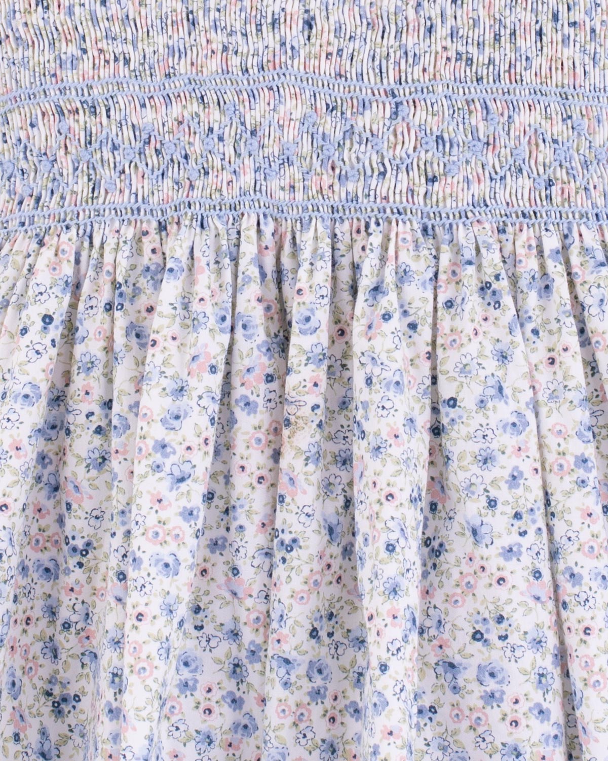 Close-up of the hand-smocked bodice and top portion of the gathered skirt of the Amandine Florencia Blue Floral Dress, highlighting the detailed blue and light blue stitching.