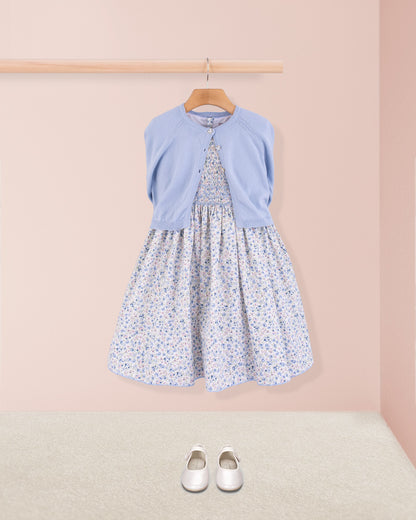Amandine Florencia Blue Floral Dress styled with a light blue cardigan and white Mary Jane shoes, displayed together on a soft pink background.