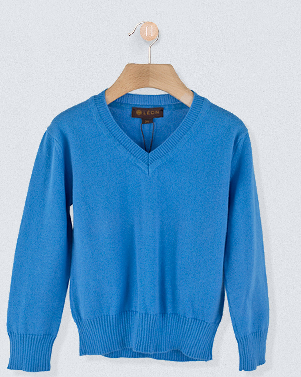 Front view of the Arnaud Cotton Sweater in perriwinlkle with a V-neckline and ribbed cuffs and hem hanging on a wooden hanger