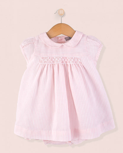 Front view of Baby Eva 2-piece outfit featuring a pink and white striped linen dress with delicate smocking and cap sleeves, displayed on a hanger against a soft pink background.