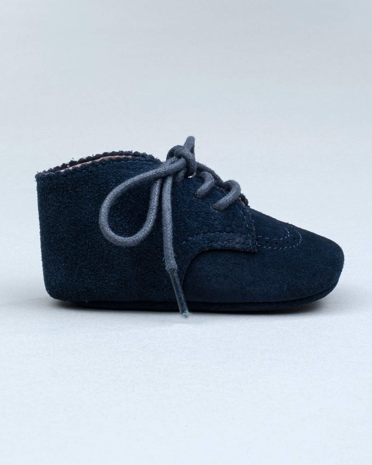 Side view of a single navy suede baby shoe with brogue stitching and lace-up closure.