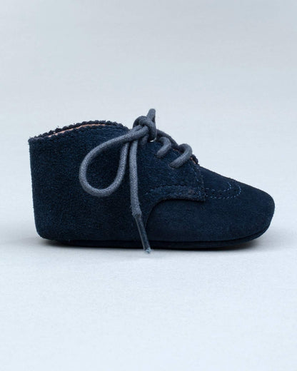 Side view of a single navy suede baby shoe with brogue stitching and lace-up closure.