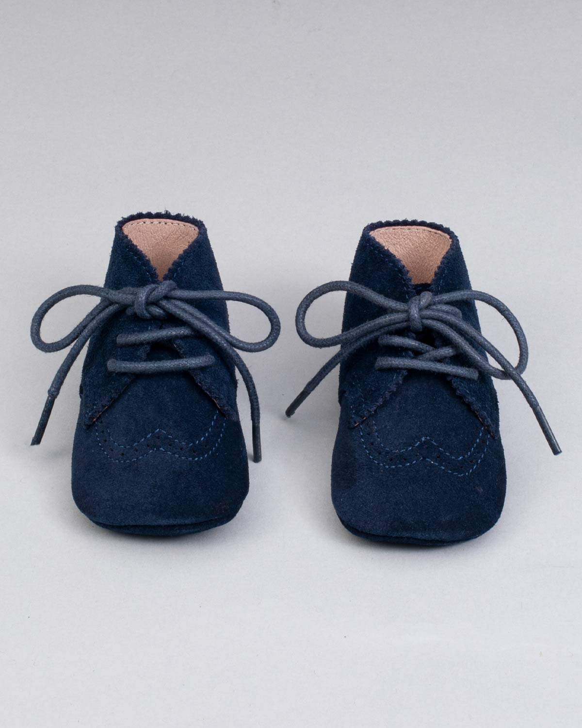 Front view of a pair of navy suede crib shoes with tied laces and scalloped brogue details.