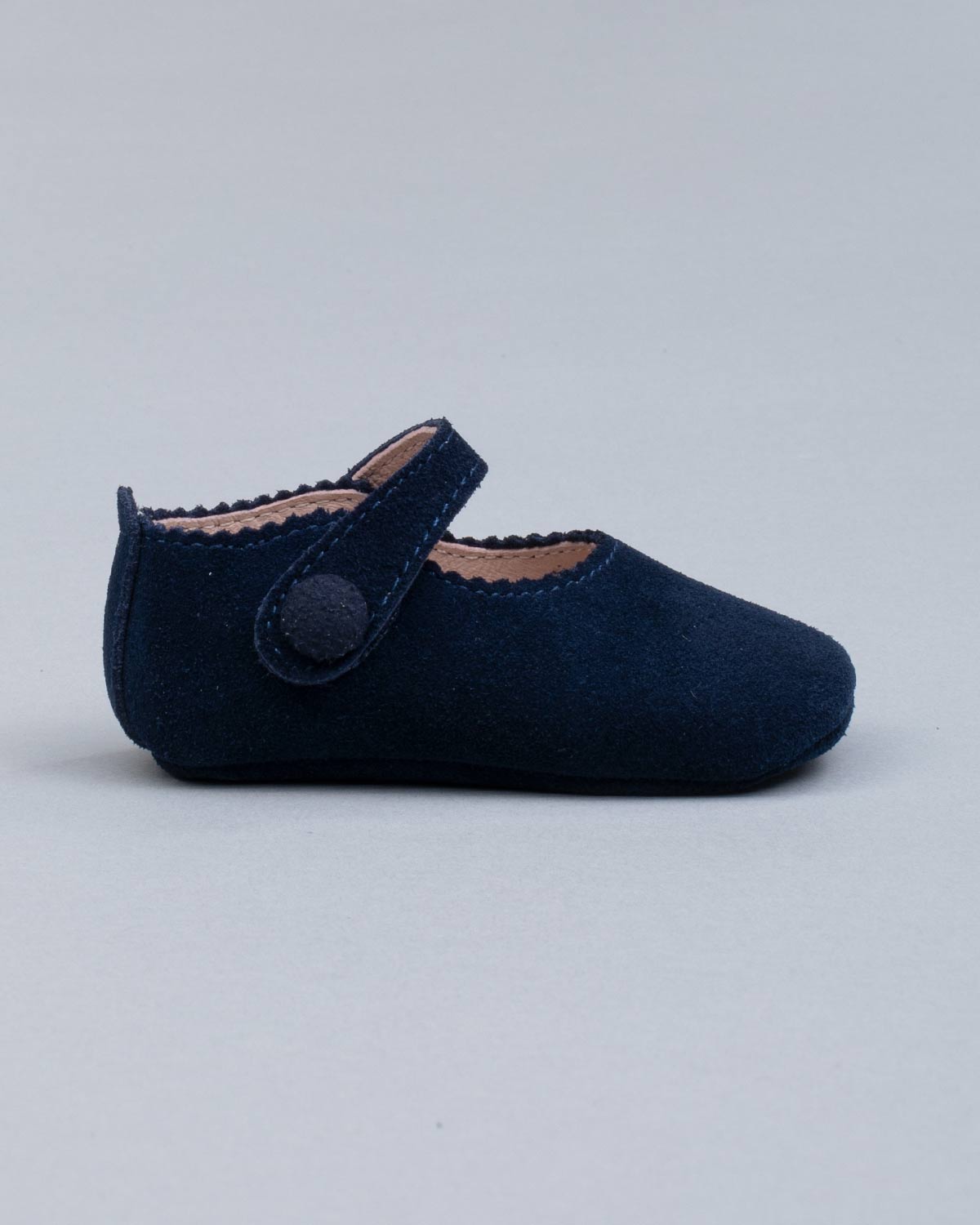 Side view of a navy suede baby crib shoe with scalloped edge and velcro strap, shown against a pale grey backdrop.