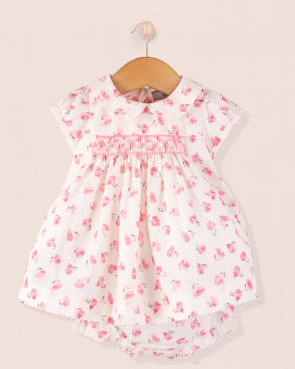 Baby Eva Versaille Rose Octuouse dress set displayed on a hanger, showing the front of the white dress with pink floral print and smocking detail at the chest, matched with a diaper cover.