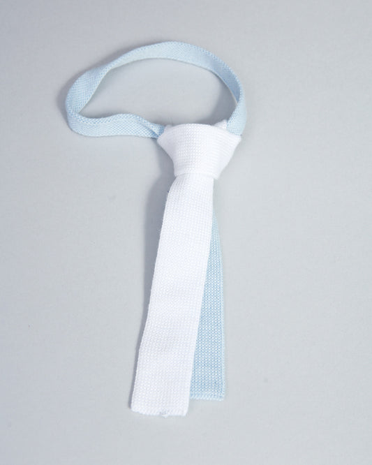 White and light blue Italian cotton knit baby tie displayed against a soft gray background.
