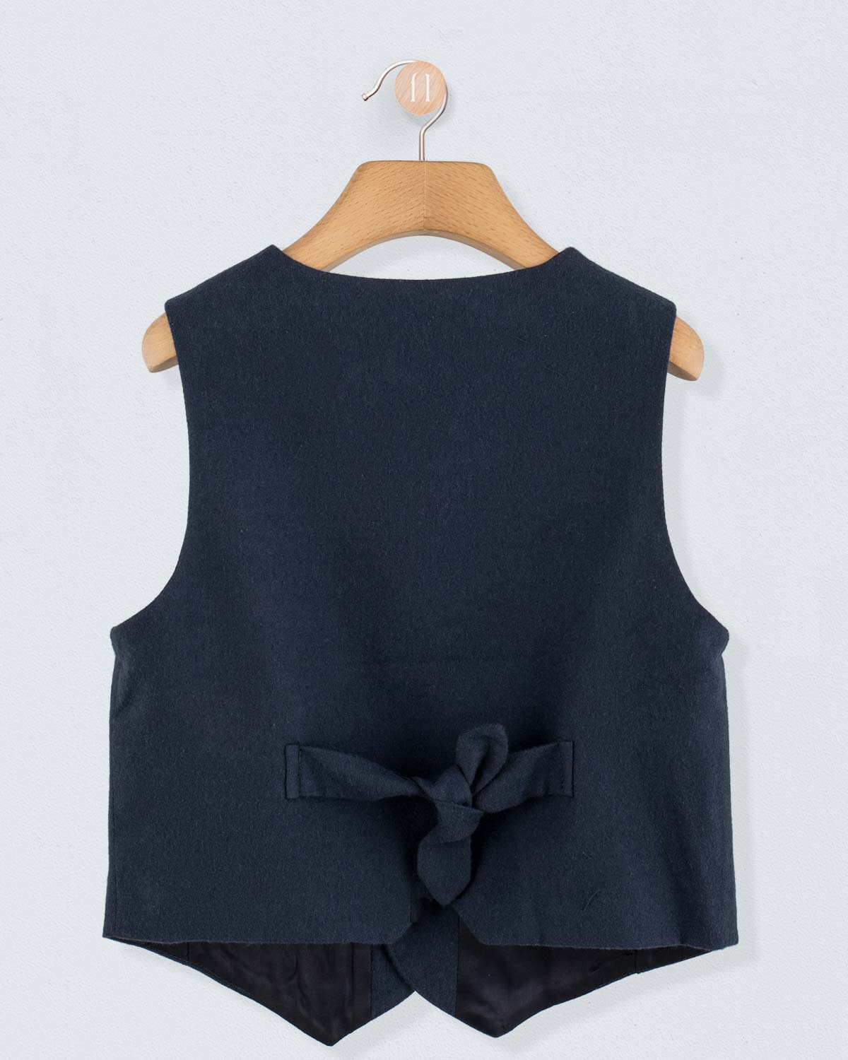 Back view of navy virgin wool vest featuring a bow tie detail, hung on a wooden hanger