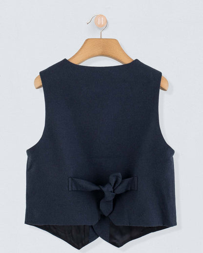 Back view of navy virgin wool vest featuring a bow tie detail, hung on a wooden hanger