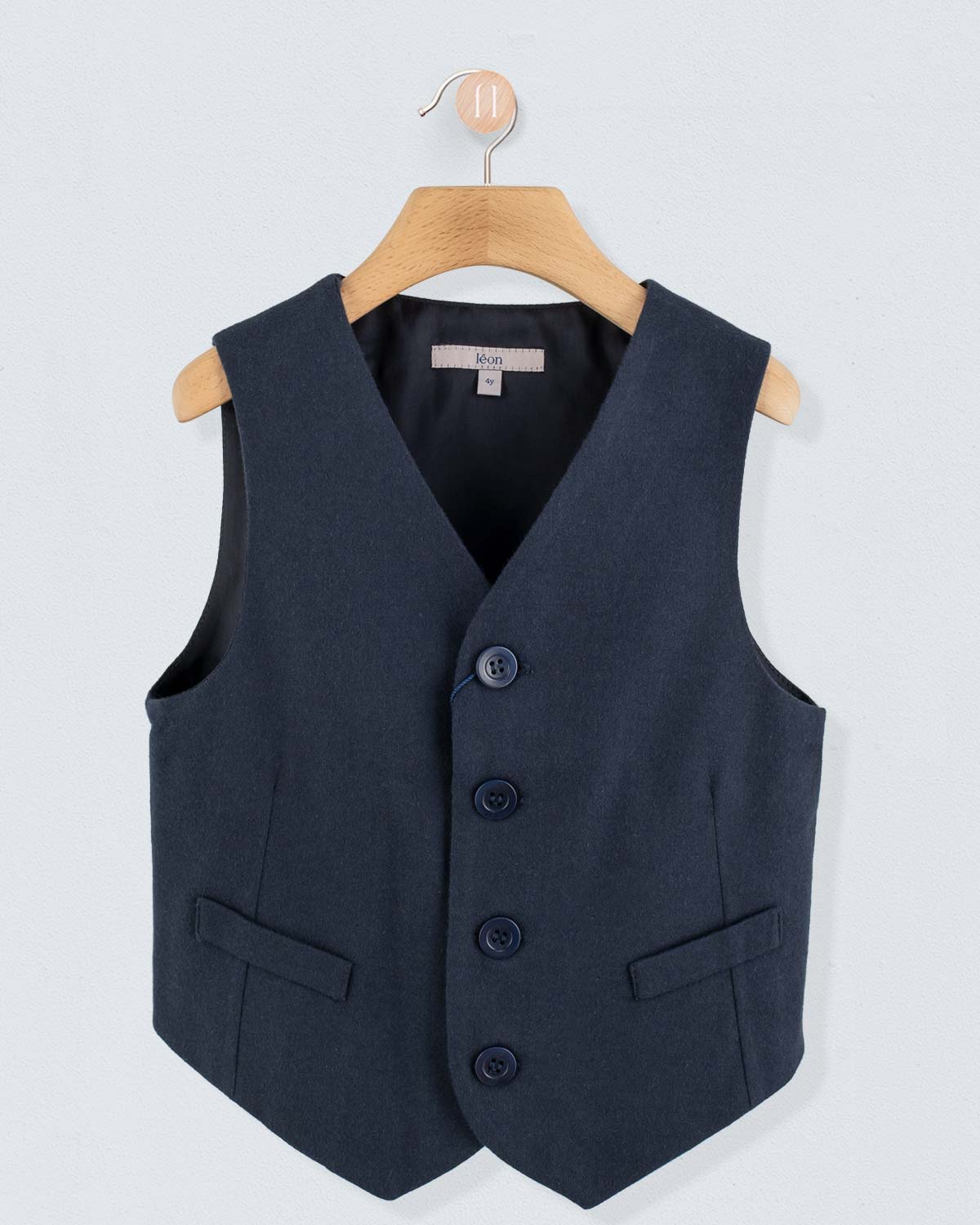 Navy virgin wool vest, displayed on a wooden hanger against a light background