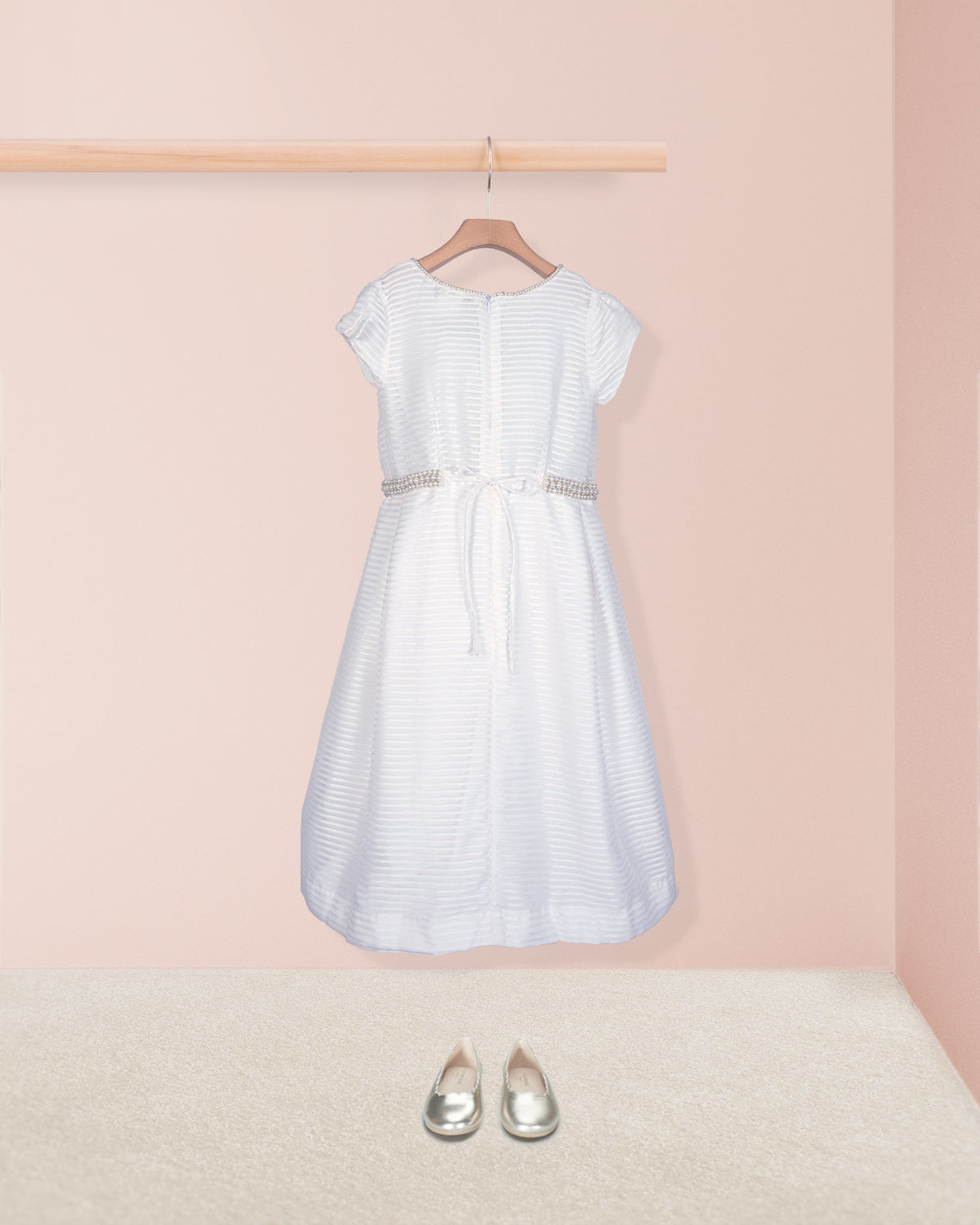 Back view of the Angelica White Organza Gown styled with silver shoes placed on the floor in a pale pink room