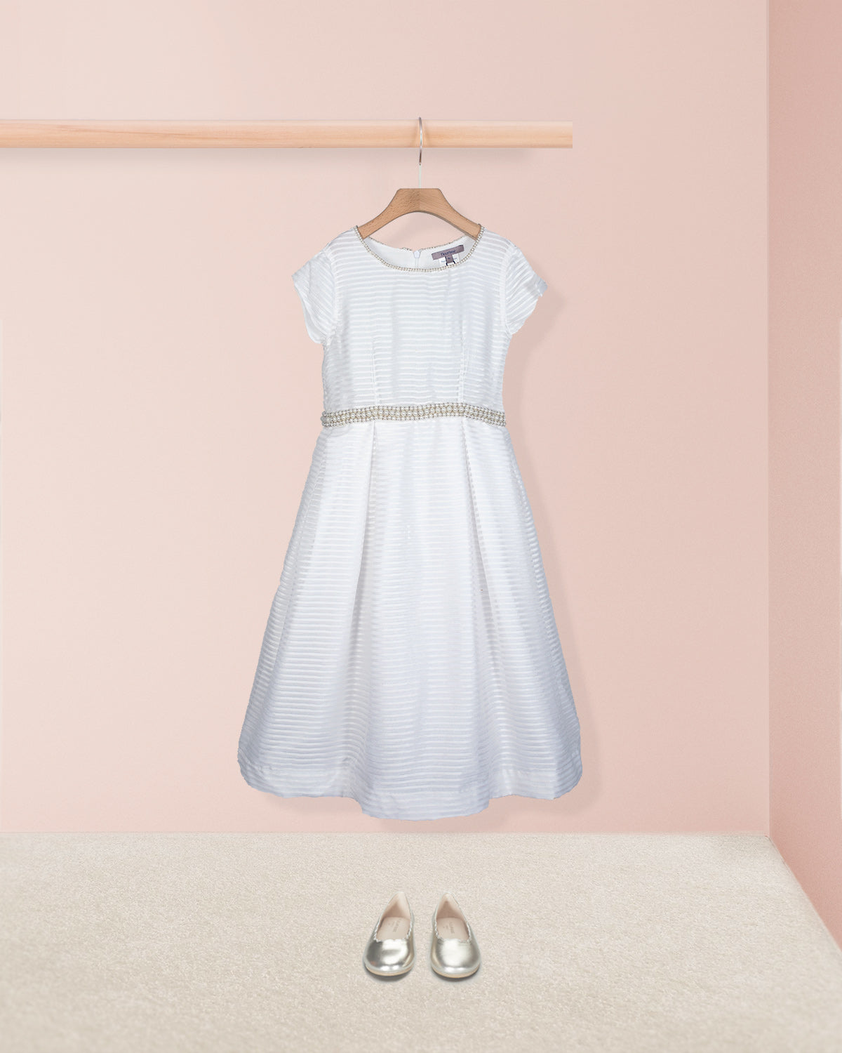 Front view of the Angelica White Organza Gown styled with silver shoes on the floor shown against a pale pink background