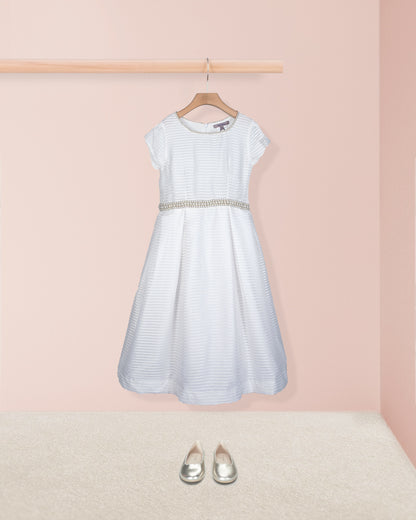 Front view of the Angelica White Organza Gown styled with silver shoes on the floor shown against a pale pink background