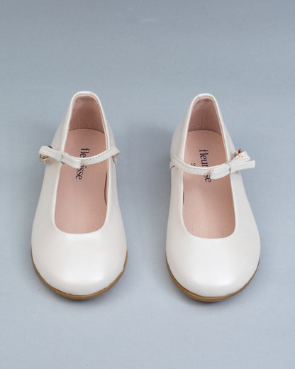 Frontal view of cream leather Mary-Jane shoes for children, showcasing symmetrical bows and rounded toes on a flat background.