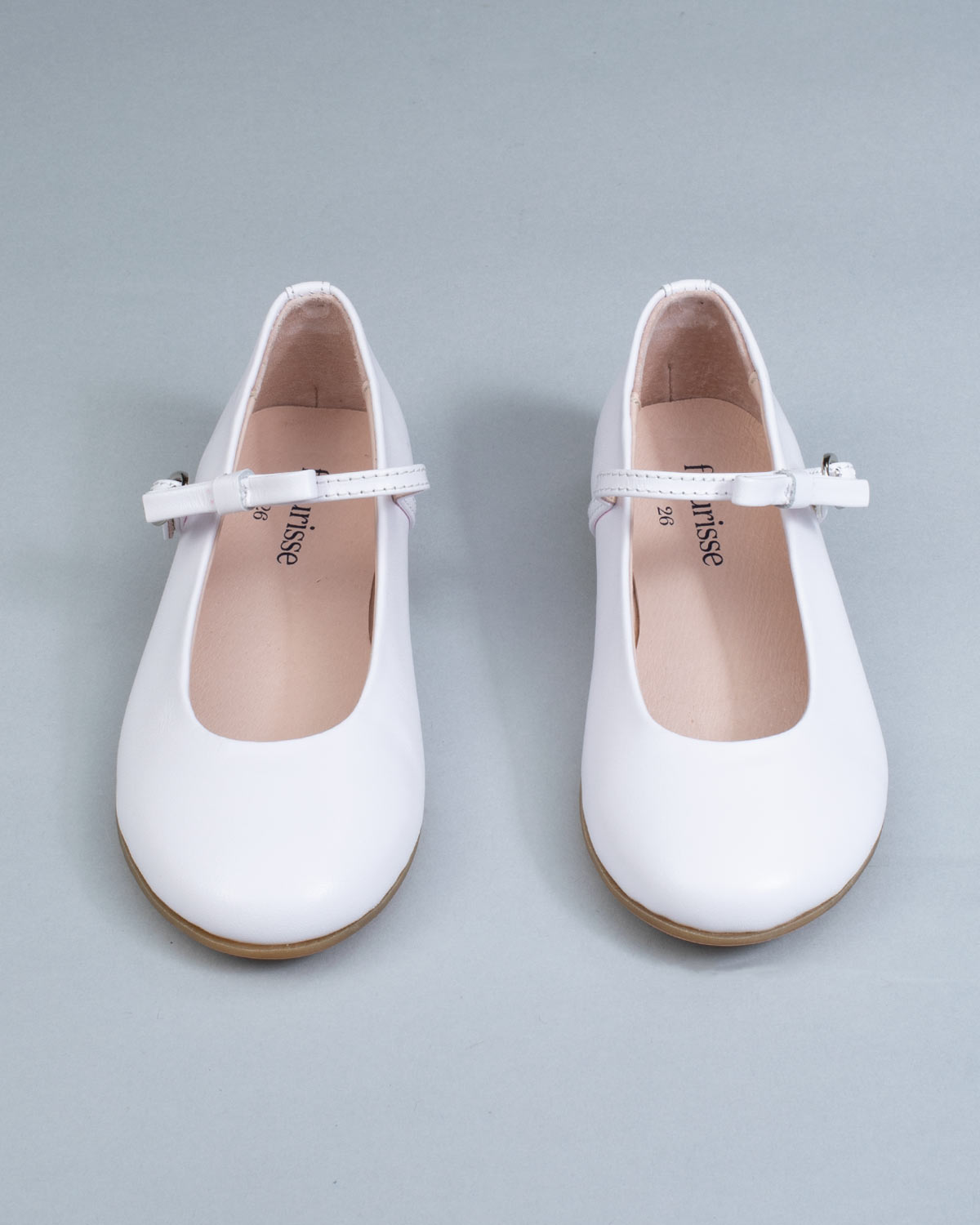 Frontal view of white leather Mary-Jane shoes for children, showcasing symmetrical bows and rounded toes on a flat background.