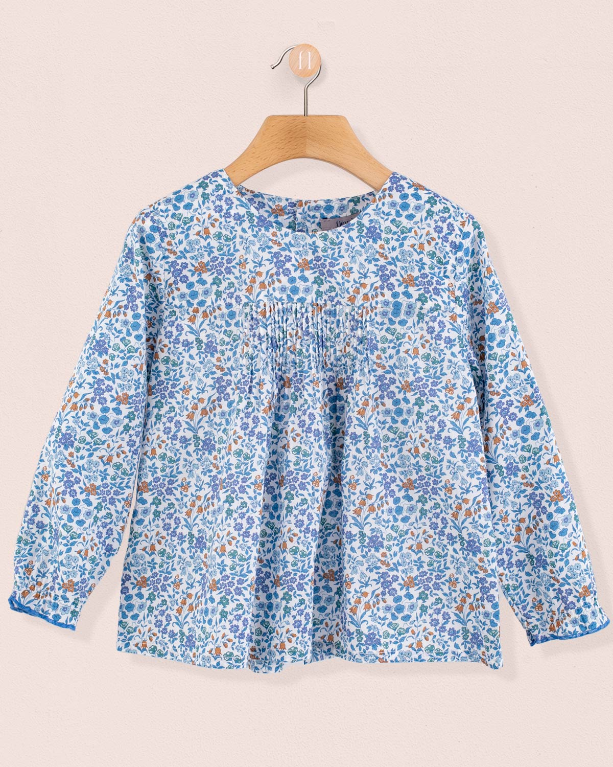 Long-sleeve floral tunic in Liberty Lillibet Blue print with front pin-tucks, hanging on wooden hanger