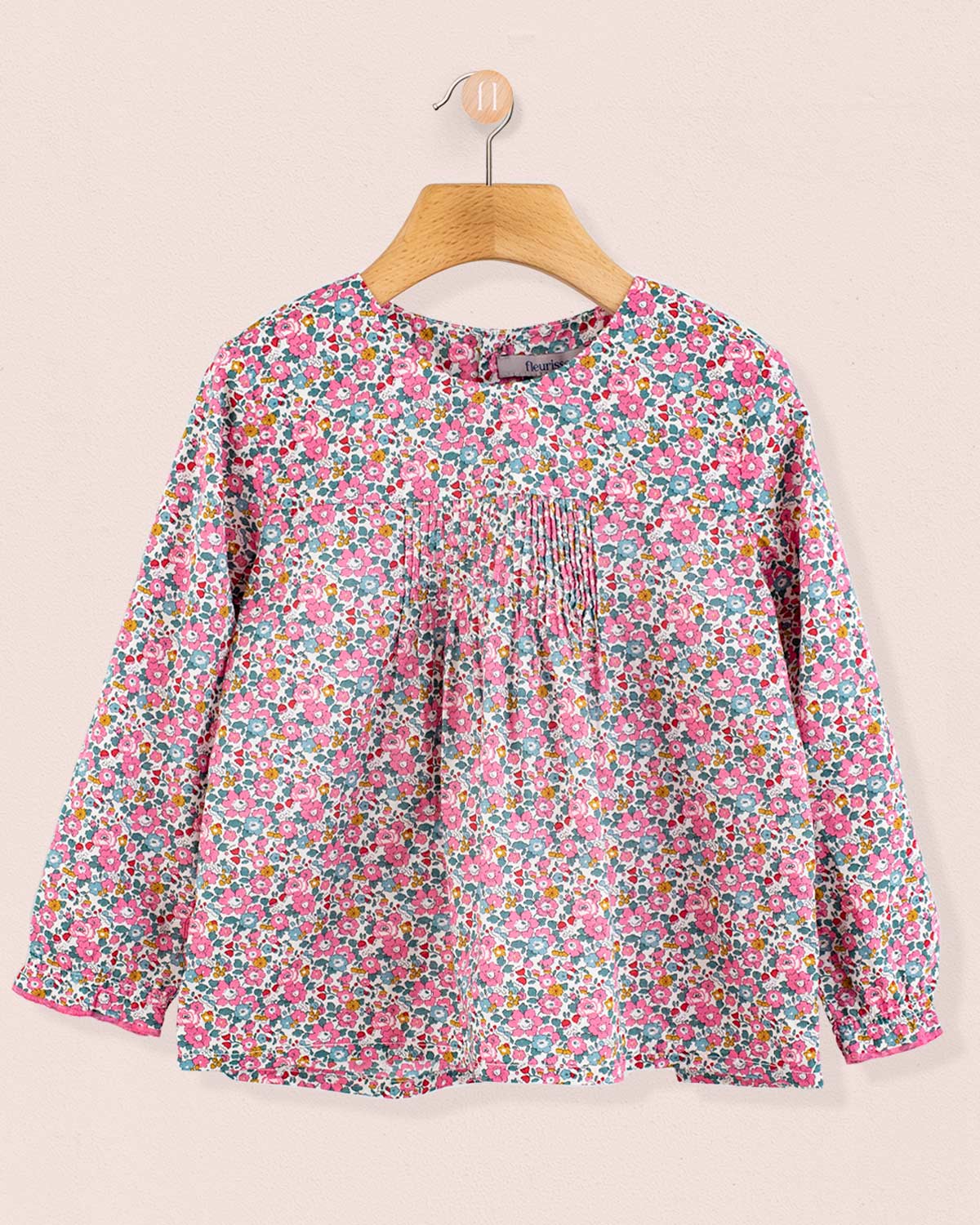 Long-sleeve floral tunic in Liberty Betsy Ann print with front pin-tucks, hanging on wooden hanger