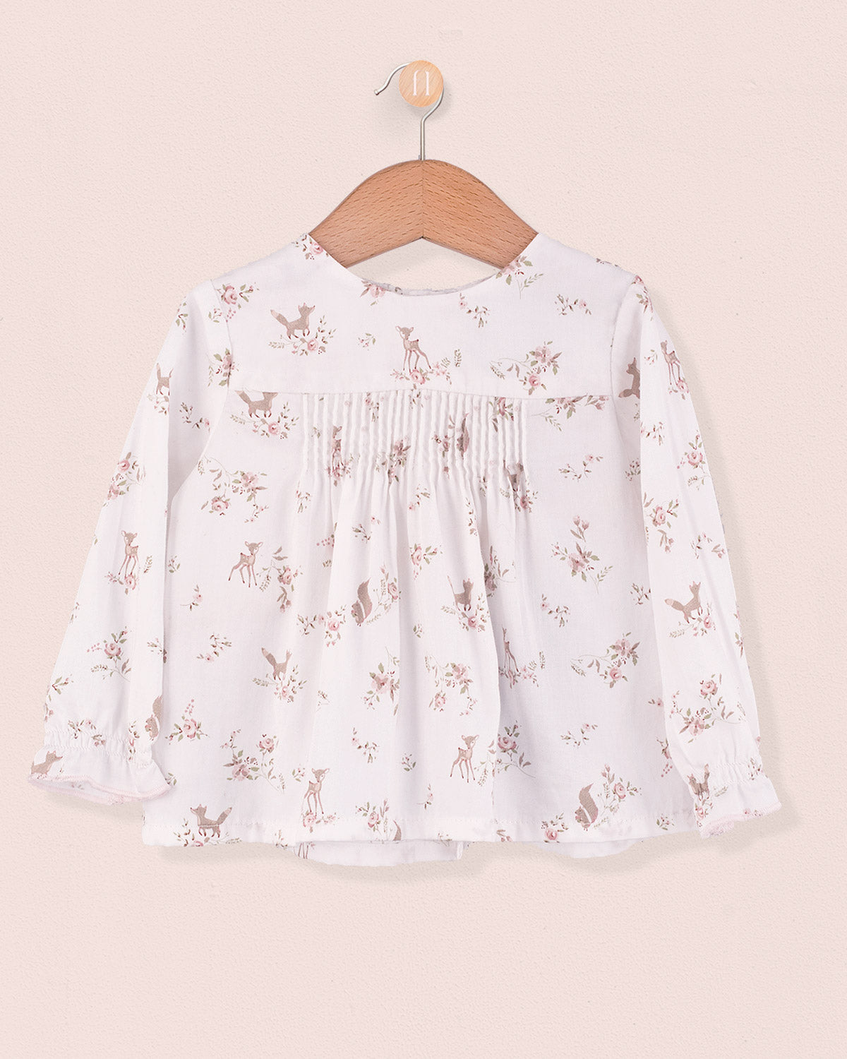 Long sleeve white tunic with pink deer and floral print, pin-tuck details on chest, hanging on wooden hanger