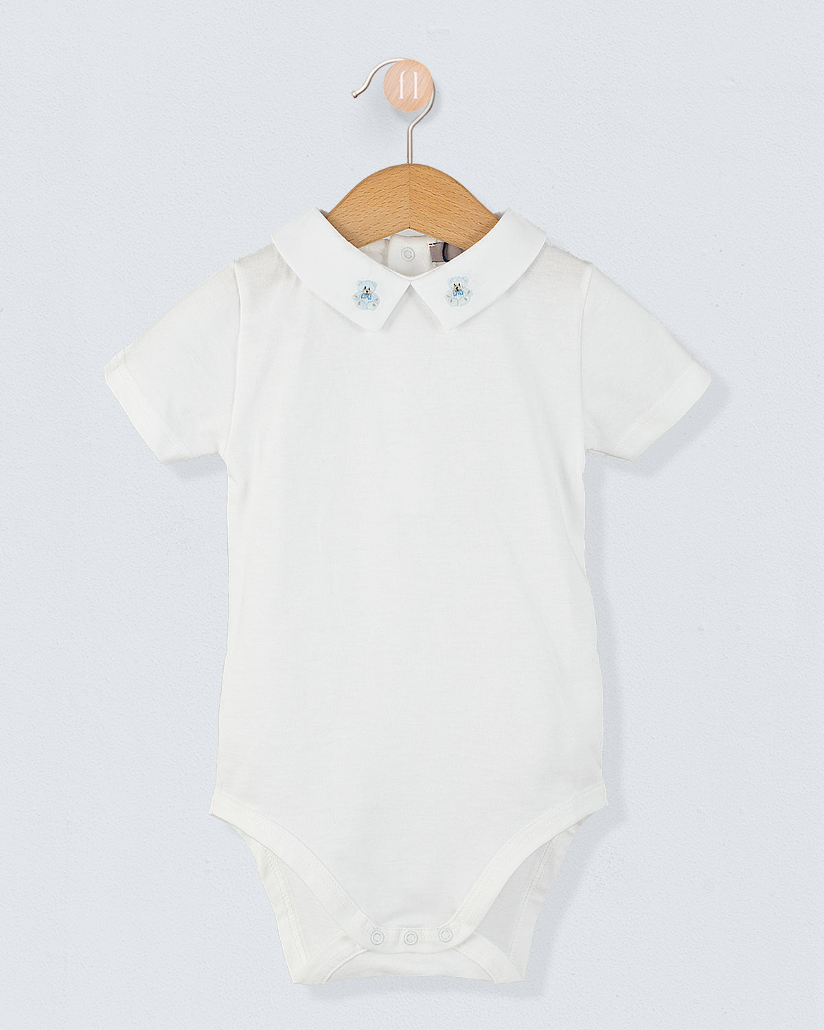 Front view of the Andreas Baby Onesie, a short-sleeve white cotton jersey bodysuit with a pointed collar featuring embroidered light blue teddy bears.