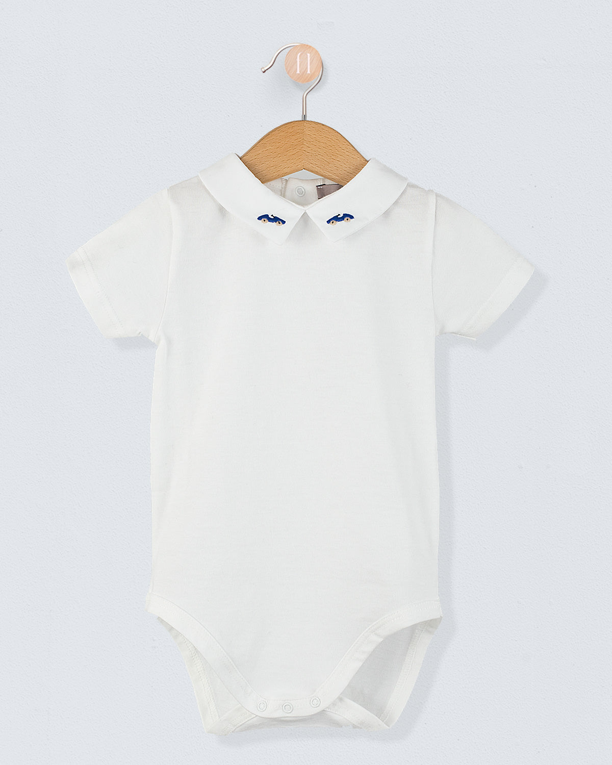 Front view of the Andreas Baby Onesie, a short-sleeve white cotton jersey bodysuit with a pointed collar featuring embroidered royal blue cars.